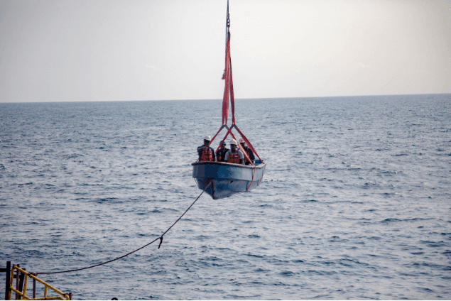 Crew in a blue lifeboat being crane-lifted over open sea
