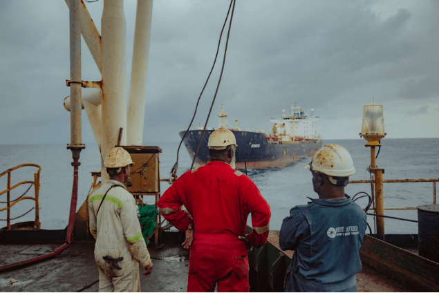 Three crew members looking out toward a tanker from the deck