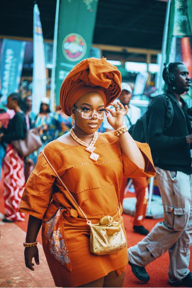 Woman in ochre gele adjusting pearl-framed glasses