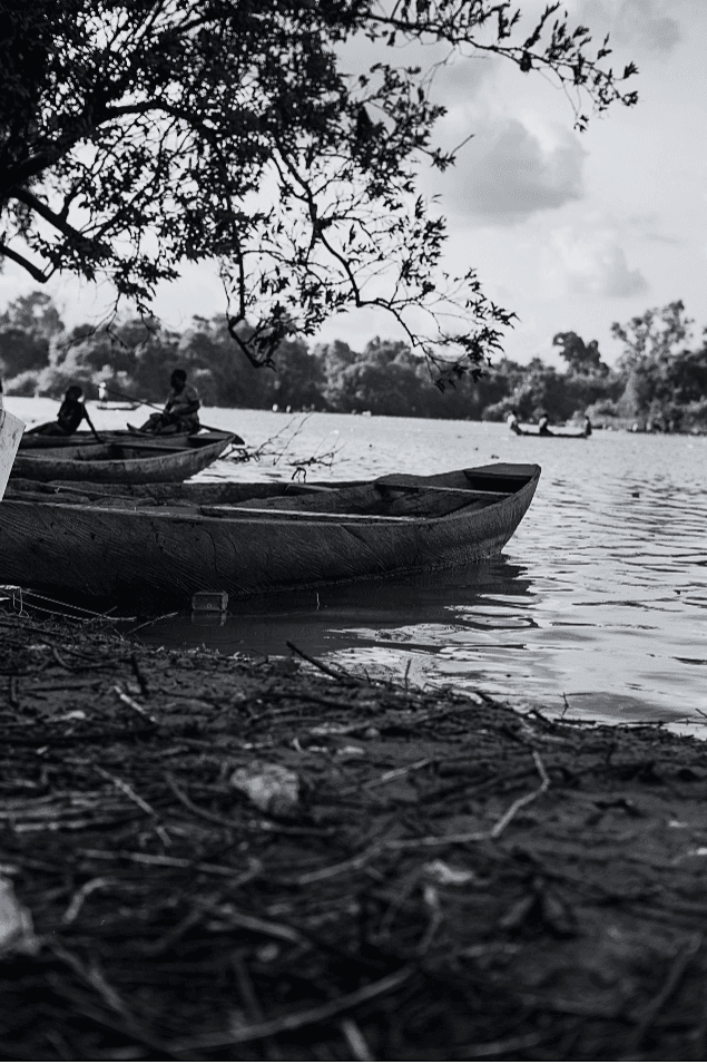 Black-and-white river scene with dugout canoes framed by branches
