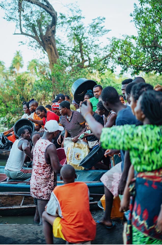 Crowd gathering at the riverbank around a blue boat